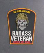 Veterans Day 2025 DCFD Badass Veteran PVC patch collection with glow-in-the-dark text featuring tactical skull design and American flag background with saluting soldiers silhouette