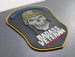 Veterans Day 2025 MPDC Badass Veteran PVC patch collection with glow-in-the-dark text featuring tactical skull design and American flag background with saluting soldiers silhouette